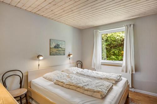 a bedroom with a bed with white sheets and a window at Lærke-huset in Bindslev
