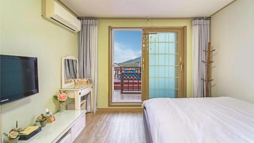 a bedroom with a bed and a television and a balcony at Geoje Araon Pension in Geoje