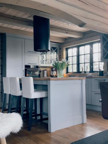 a kitchen with white cabinets and a island with white chairs at Koslig helårs hytte in Heimdal