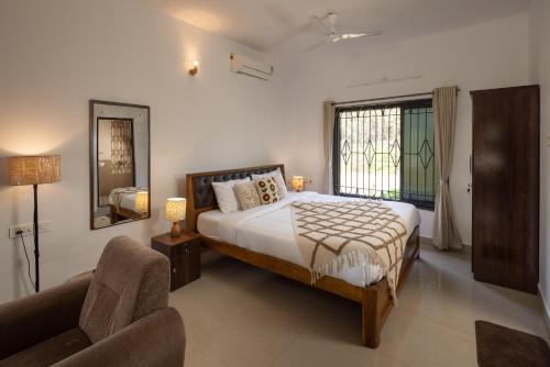 a bedroom with a bed and a chair and a window at Palolem White House in Canacona