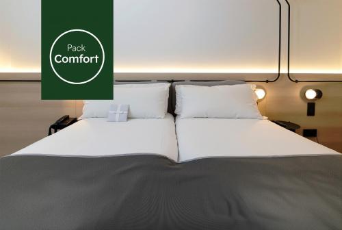 a bed with white pillows and a green sign that reads pack comfort at Sercotel Delfos Andorra in Andorra la Vella