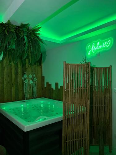 a hot tub in a room with green lighting at Hédoné LoveRooms in La Chapelle