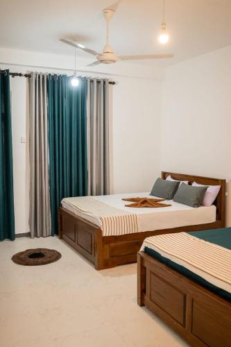 two beds in a bedroom with green curtains at Rainforest White House in Deniyaya