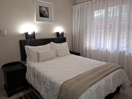 a bedroom with a bed with white sheets and a window at #7 Illovo Views in Kingsborough