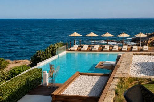 a swimming pool next to the ocean with chairs and umbrellas at Palmalife Bodrum Resort & Spa in Yalıkavak