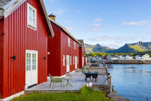 a red building with a deck next to a body of water at Astra Village - Waterfront Rorbu Cabins in Lofoten in Kabelvåg