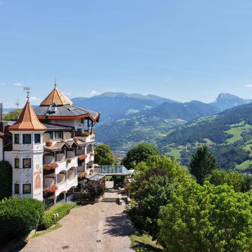 a building on a hill with mountains in the background at Granpanorama Hotel StephansHof in Villandro