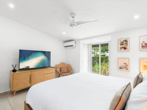 a white bedroom with a large bed and a tv at Shell Beach Splendide 2 chambres sur la plage in Baie Nettle