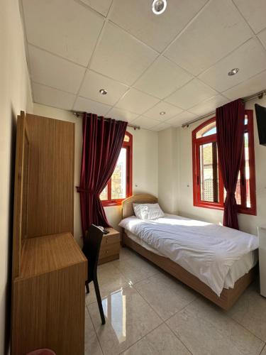 a bedroom with a bed and a desk and two windows at Hotel St Jean in Zahlé