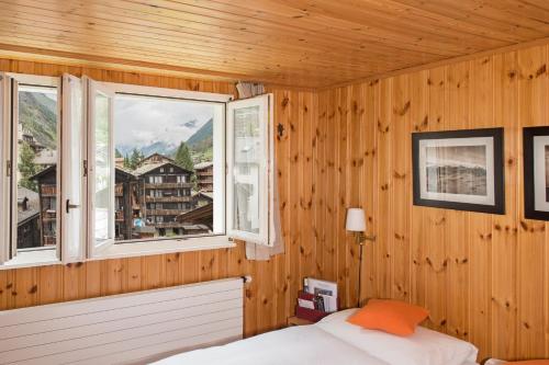 a bedroom with a bed and two windows at Hotel Alpina in Zermatt