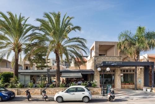 a white car parked in front of a hotel with palm trees at Elotis Suites in Agia Marina Nea Kydonias