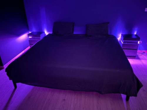 ein Schlafzimmer mit einem schwarzen Bett und violetten Lichtern in der Unterkunft Love room l'Evasion in Esprels
