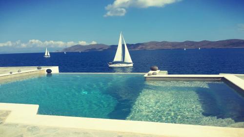 a man sitting in a swimming pool with a sailboat in the water at Cape Villa at Sounio in Sounio