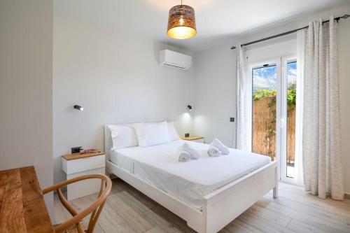 a white bedroom with a bed and a window at MENTOROS VILLAS in Karavádhos