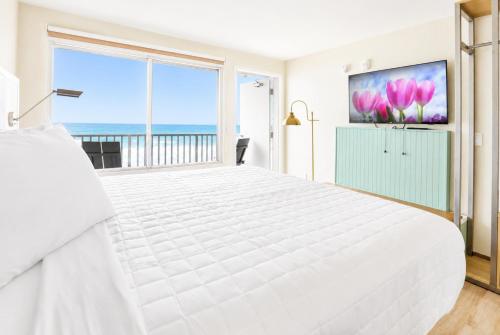 a white bedroom with a large bed and a large window at Palm & Tide Beachfront Hotel in Panama City Beach