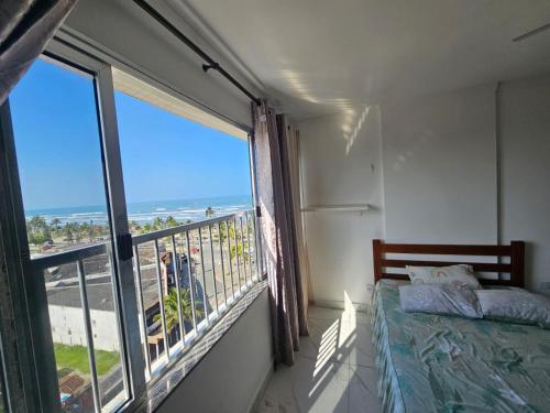a bedroom with a large window with a view of the beach at Apartamento em Peruíbe (Centro) in Peruíbe