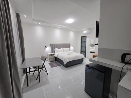 a white bedroom with a bed and a table and a chair at SADO Guesthouse in Katima Mulilo