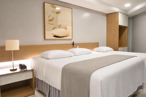 a bedroom with a large white bed and a lamp at Treville Hotel in Caràzinho