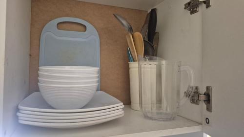 a shelf with plates and a container of utensils at Residencial Acropolis in Sonsonate