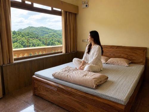 a woman sitting on a bed looking out a window at Bavieco Resort in Yên Bài