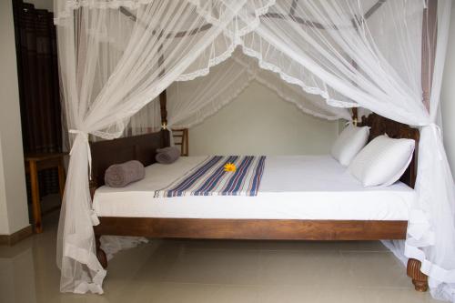 a bedroom with a canopy bed with white drapes at Minara Guest House in Mirissa