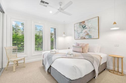 a bedroom with a bed and a chair and windows at Whitepepper Cottage in Pokolbin