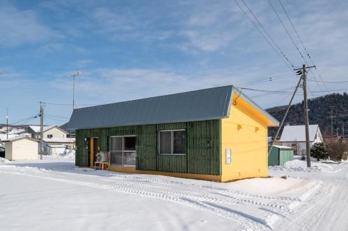 a small green and yellow building in the snow at c Furano A in Furano