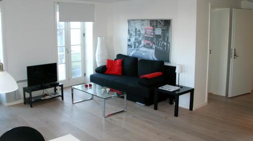 uma sala de estar com um sofá preto e uma televisão em Badepensionat Sandloppen - Ferielejligheder em Allinge