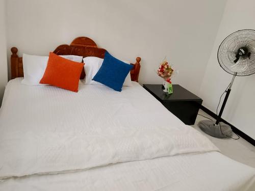 a white bed with colorful pillows and a fan at Ciao Villa, Kandy in Kandy