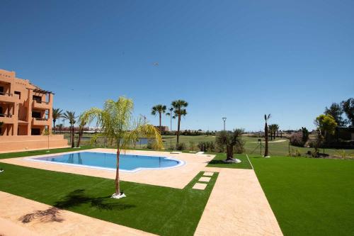 a swimming pool in the middle of a lawn with palm trees at Serena Golf Apartments in Los Alcázares
