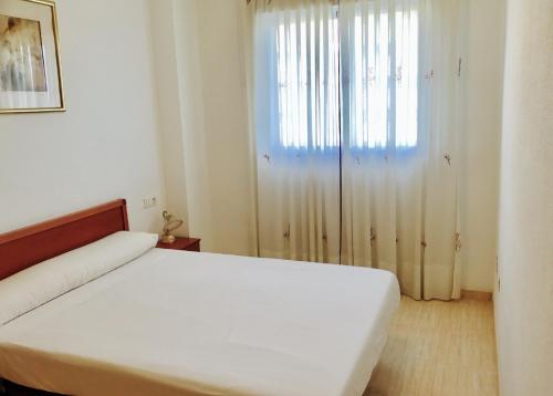 1 dormitorio con cama blanca y ventana en Apartamento Caribe Playa, en Oropesa del Mar