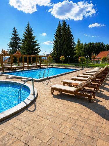 a large swimming pool with wooden benches and a row of tables at Deluxe Mountain View Studio ViS in Residence Hill Hotel Kopaonik in Kopaonik