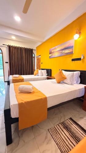 two beds in a hotel room with yellow walls at Secret Garden Beach Hotel in Trincomalee