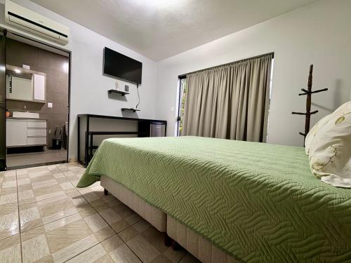 a bedroom with a green bed and a television at Suíte Gute Nacht 3 in Pomerode