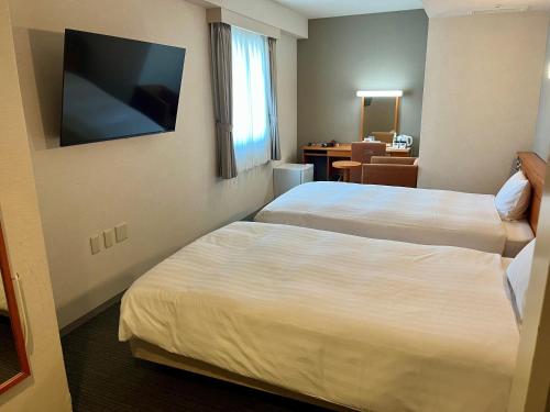 a hotel room with two beds and a flat screen tv at Hotel Premium Green Plus in Sendai