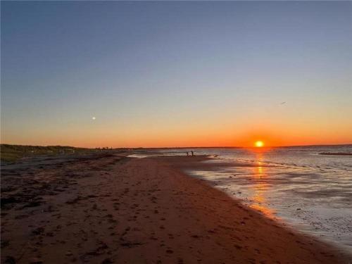a beach with the sun setting in the ocean at Private Beach Escape - Chalet Ferdinand in Grand Barachois