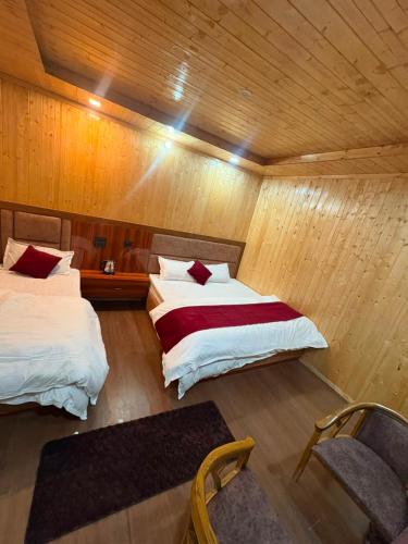 two beds in a room with wooden walls at Harshil wood stay in Harsil