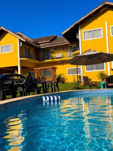 a swimming pool in front of a house with an umbrella at Villa das Calliandras in Chapada dos Guimarães