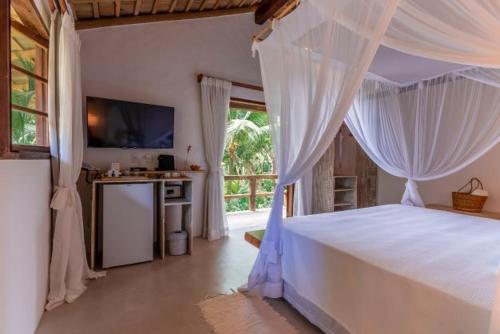 a bedroom with a bed with white curtains and a television at DA GRAÇA HOTEL in Trancoso