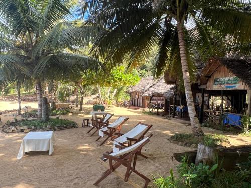 a group of tables and chairs on a beach with palm trees at Lokobe Djema Forest Lodge in Nosy Be