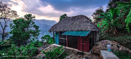 a small hut with a thatched roof on a mountain at The Cloud door in Perumālmalai