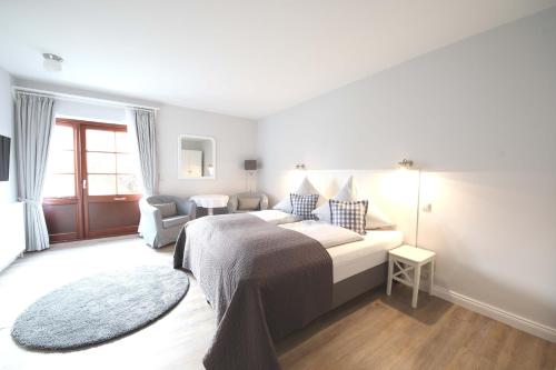 a white bedroom with a bed and a chair at Landhaus Nordstern Hotel garni in Utersum