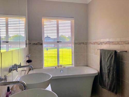 a bathroom with two sinks and a tub and two windows at Beautiful 3 bedroom flat in Grahamstown