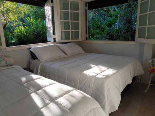 two beds in a room with two windows at Ecos Jatobá - Refúgio à 12 km do Santuário de Aparecida in Guaratinguetá