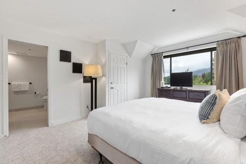 a white bedroom with a large bed and a window at Powder's Edge by Whiski Jack in Whistler