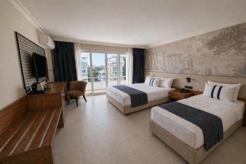 a hotel room with two beds and a desk and a television at TRYP by Wyndham Didim in Didim
