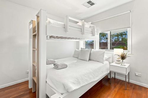 a white bedroom with a bunk bed and a window at Coast Bliss on Currambene in Huskisson
