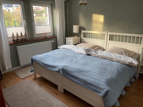 a bedroom with a bed with a blue blanket and two windows at Zimmer Mühlenbach, ein Zimmer in FeWo mit 2 Zi in Schieder-Schwalenberg