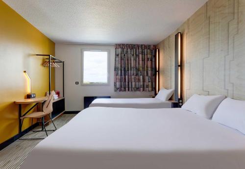 a bedroom with two beds and a desk and a window at B&B HOTEL Reims Tinqueux in Reims