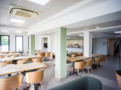 a dining room with wooden tables and chairs at BRIT HOTEL CONFORT Roissy Saint-Witz in Saint-Witz